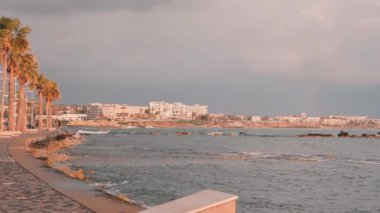Baf rıhtımı. Kıbrıs'ta turist gezinti. Pembe alacakaranlıkta turist bölgesi. Rocky Beach boyunca çekici erkek koşucu eğitim. Akdeniz kıyıları. Arka planda oteller ile Fırtınalı deniz. Yavaş çekim