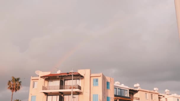 空に虹。雨上の虹。嵐の後の虹の出現。悪天候時の灰色の曇り空。前面に建物を持つカラフルな曲線 — ストック動画