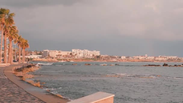 帕福斯码头。塞浦路斯的旅游长廊。粉红色黄昏的旅游区。有吸引力的男性跑步者沿着岩石海滩训练。地中海沿岸。暴风雨的海洋与酒店的背景。慢动作 — 图库视频影像