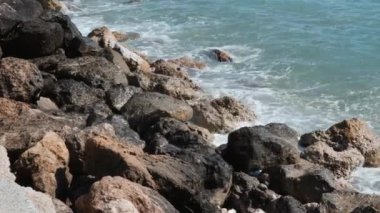 Büyük deniz dalgaları ile taşların yakından görünümü. Kayalık sahile çarpan dalgalar. Masmavi deniz suyu kayalık kıyıya çakılıyor. Dalgalar sıçrama ve köpük oluşturma
