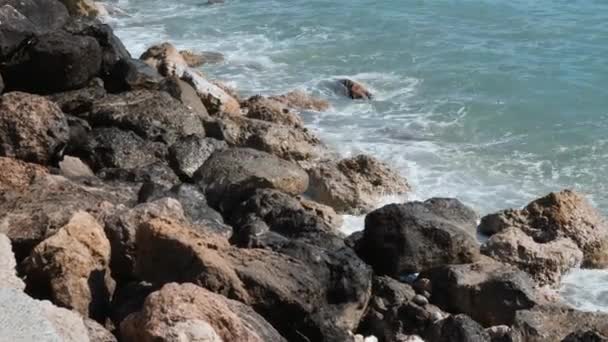 Büyük deniz dalgaları ile taşların yakından görünümü. Kayalık sahile çarpan dalgalar. Masmavi deniz suyu kayalık kıyıya çakılıyor. Dalgalar sıçrama ve köpük oluşturma — Stok video