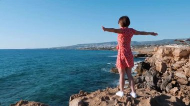 Denizle çevrili uçurumun kenarında duran genç kız. Beyaz elbiseli beyaz kız, uçurumun kenarında durup denize bakıyor. Kız yanlara uzanmış kolları ile kayalık kayalık üzerinde duran