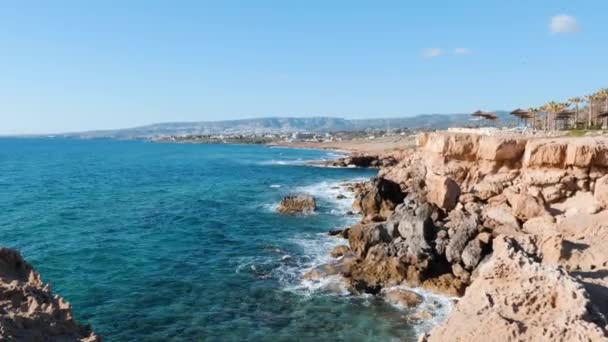 Side view of rocky seashore. Rocky cliffs with clear azure water. Edge of cliff surrounded by sea. Sea waves hitting rocky shore. — Stock Video