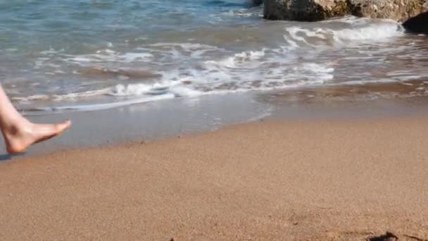 Тонкі ноги жінки ходять на жовтому піску вздовж моря. Тонкі таніровані ноги на пляжі з піском. Молода струнка дівчина йде уздовж моря і залишає сліди піску . — стокове відео