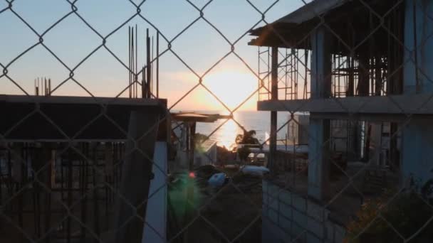 Construcción de cabañas en el fondo del atardecer. Filmación de la construcción a través de valla. Construcción de villas al atardecer . — Vídeo de stock