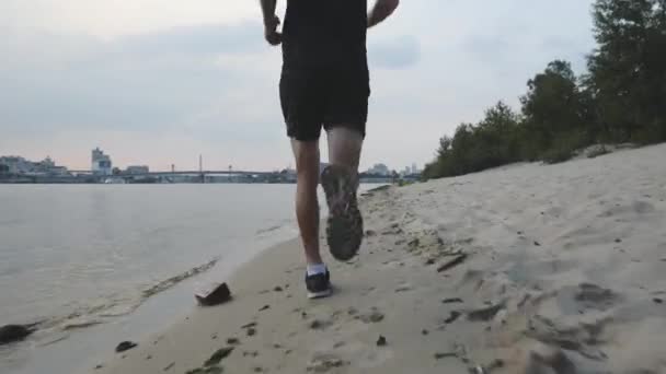 Muscular powerful male legs runs along river beach.  Follow view of slim male legs jogging near river in evening. Young fit boy training near river. Close up of strong male legs running along creek — Stock Video