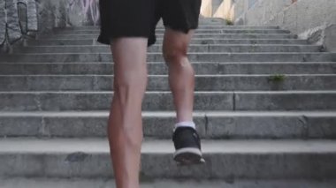 Güçlü ince erkek bacakları merdivenlerden yukarı koşuyor. Atletik güçlü tabaklanmış bacaklar adımlar kadar çalışır. Kaslı erkek bacaklarının arka görünümüne yakın. Genç aktif çocuk adımlarla hızlı koşuyor. Yavaş çekim