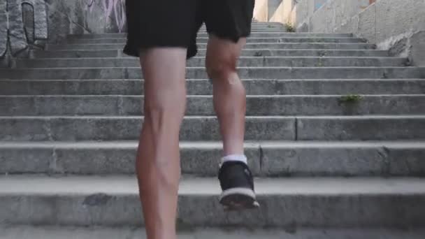 Powerful slim male legs running up stairs. Athletic strong tanned legs runs up steps. Close up back view of muscular male legs. Young active boy running fast on steps. Slow motion — Stock Video