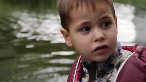 Retrato de un niño lindo con agua en el fondo. Vista de cerca de la cara de niño adorable. Cara de niño pequeño con agua verde sobre fondo. Retrato de niño feliz en el lago — Vídeos de Stock