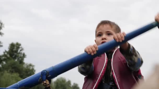 Portrét malého šťastného dítěte, který drží modrý dřevěný veslo na jezeře v parku. Malý rozkošný kluk na lodi. Zavřete zobrazení. Šťastný chlapec se usmívá v kameře a mluví se svou matkou — Stock video