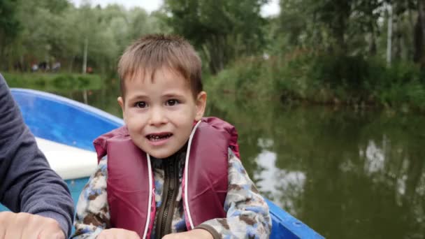 Portrét malého roztomilého dítěte drží pádlo. Zblízka pohled na malého roztomilým chlapečka, který se usmívá na jezero. Šťastné dítě drží pádlo a mluví na kameře v parku. — Stock video