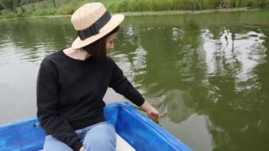 Hasır şapkalı kadın elini suya tutar. Gölde teknede dinlenen mutlu kız. Kameraya gülümseyen kadın. Kız suya palmiye yol açar. Kadın el yavaşça gölde su yüzeyine dokunur