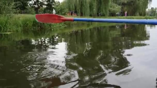 Сходи над водою. Червоно-синій весло, піднятий над водою на озері в міському парку. Краплі води течуть вниз — стокове відео