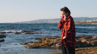 Kötümser kadın deniz kıyısında duruyor ve üşüyor. Yalnız kadın rüzgarlı sonbahar gününde sahilde donuyor. Deniz ufkuna bakan üzgün bir kadın. Kadın üzgün. Melankoli kadın kırmızı gömlek kendini sarar