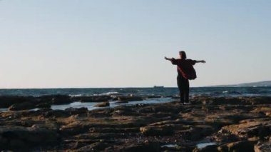 Genç çekici kadın kıyı kenarında duran ve ufuk bakıyor. Elleri yanlara doğru kaldıran mutlu kadının arka görünümü. İlham olumlu fikirli kadın sahilde ayakta yana ellerini kaldırdı