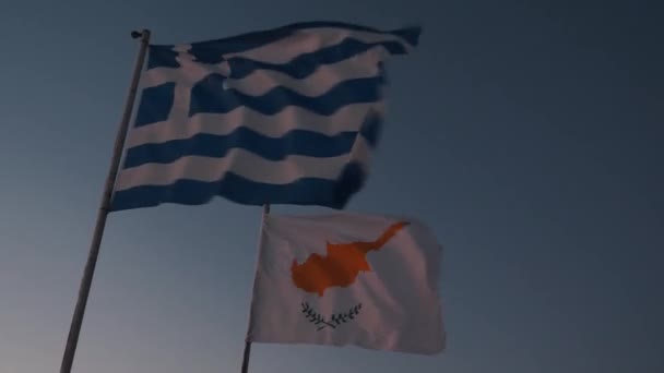 Lähikuva näkymä Kypros ja Kreikan liput heiluttaa tuulessa vastaan sininen taivas. Kypros ja tervehtimään lippuja auringonlaskun taivaalla — kuvapankkivideo