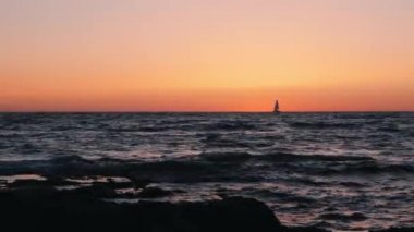 Ufukta küçük yelkenli ile inanılmaz turuncu gün batımı. Gün batımında denizde yüzen küçük yelkenli silueti. Denizde yelkenli silueti. Alacakaranlıkta yelkenli silueti.