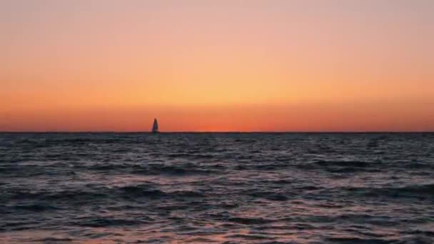 Silhouette di piccola barca a vela in crepuscolo arancione. Piccola barca a vela in mare al tramonto. Bellissimo mare calmo contro il tramonto con barca a vela all'orizzonte. Bellissimo tramonto con barca a vela all'orizzonte . — Video Stock