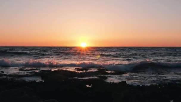 Ondas do mar contra o pôr-do-sol laranja. O sol põe-se sobre o mar bonito. Incrível pôr-do-sol laranja. Oceano ao anoitecer. Ondas do oceano atingindo a costa rochosa ao pôr do sol — Vídeo de Stock