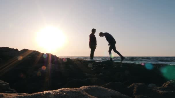 年轻的害羞的男人在日落时分在海边向心爱的女孩献情。有吸引力的人站在他的膝盖上，在日落时提出一个报价。被激怒的男人向女朋友求婚的剪影 — 图库视频影像