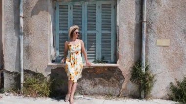 Mavi ahşap pencere ile eski evin yakınında duran ve kameraya poz yaz elbise ve güneş gözlüğü çekici esmer kadın