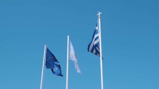 Banderas de Grecia, Chipre y la unión europea en el asta de la bandera ondeando en el viento contra el cielo azul claro — Vídeos de Stock