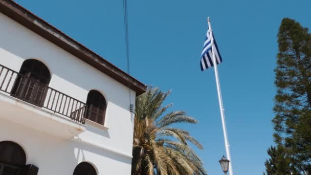 Bandera griega ondeando en viento contra el cielo azul claro. Vista inferior de parte del edificio blanco con bandera griega — Vídeos de Stock