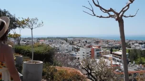Sarı yazlık elbiseli esmer kız tatil şehrinin bakış açısına geliyor ve ufukta denizi gösteriyor — Stok video