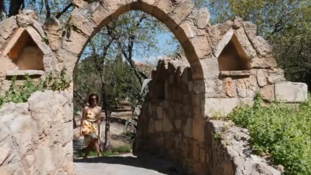 Attractive young woman in summer dress with sunflowers and straw hat walking in park with beautiful architecture — Stock Video