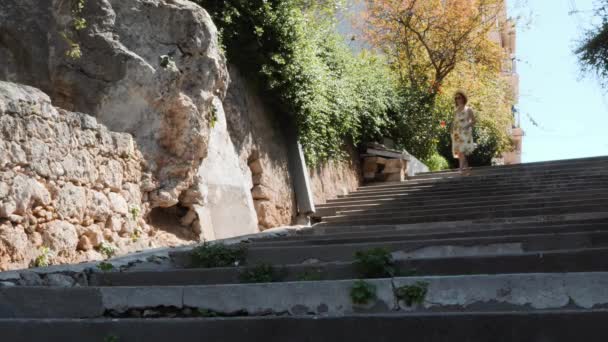 Νεαρή μελαχρινή γυναίκα σε βαμβάκι φόρεμα με ηλιοτρόπια και ψάθινο καπέλο περπατώντας στο ιστορικό μέρος της πόλης και απολαμβάνοντας τις καλοκαιρινές διακοπές — Αρχείο Βίντεο