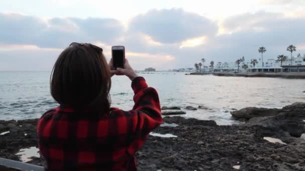 Ung brunett kvinna tar bilder av vacker solnedgång. Attraktiv kvinna stående på strandpromenaden och göra bilder — Stockvideo