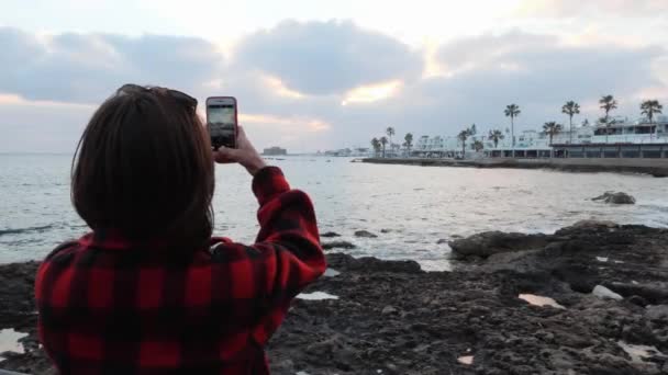 Bella giovane donna bruna in piedi sulla riva del mare e scattare foto di passeggiata turistica. Attraente femminile fare foto di banchina — Video Stock