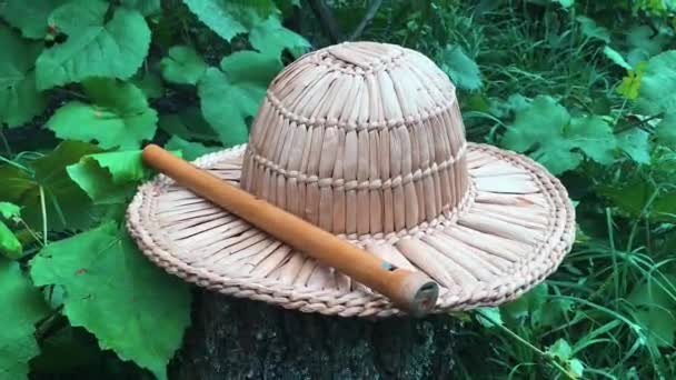 Vista cercana del sombrero de paja y la flauta de madera en el jardín verde. Instrumento de música sobre tronco de madera — Vídeos de Stock