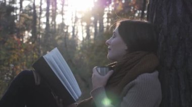Sıcak çay veya kahve fincan ıslayla ekose oturan ve gün batımına bakan genç sevimli duygusal kadın turist portresi