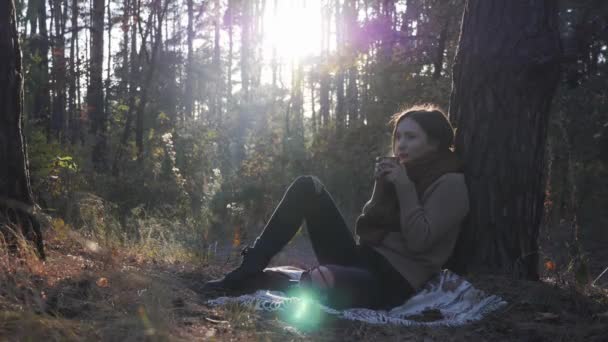 Portrait of nostalgic young woman holding hot cup of tea or coffee and drinking outdoors. Peaceful attractive female relaxing in fall forest — Stock Video