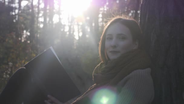Portrét mladé, dobře vypadající kavkazské ženy s knihou v podzimním lese za slunečného dne. Zblízka pohled na šťastné nostalgické samičky na podzim parku — Stock video