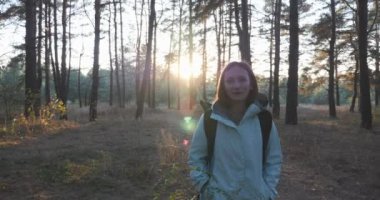 Gün batımında yeşil çamlar arasında sonbahar ormanında yürüyen büyüleyici mutlu kadın modelin ön görünümüne yakın. Ağaçlar parkta sonbahar güneşli gün zevk genç kadın