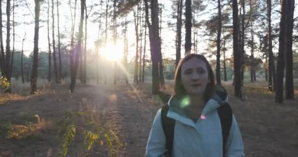 Porträt einer glücklichen, hübschen Reisenden in blauer Jacke mit großem Touristenrucksack, die bei Sonnenaufgang durch den herbstlichen Wald spaziert — Stockvideo