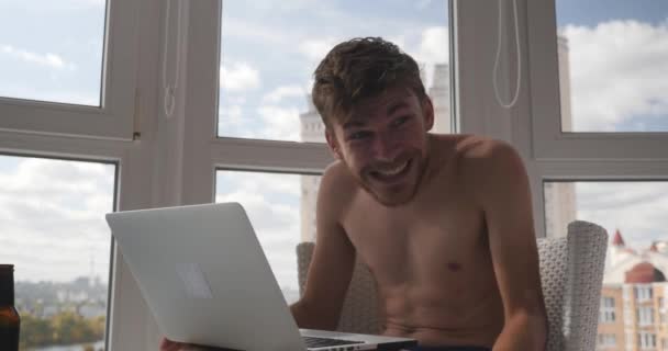 Щасливий веселий кавказький чоловічий геймер в трусиках, який грає на ноутбуці і виграв онлайн відеоігри, підняв руки і радіє — стокове відео