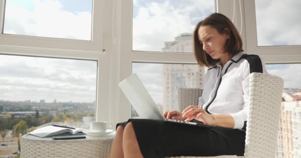 Smart successful young businesswoman in white blouse and black skirt working on laptop at working place with big windows — Stock Video