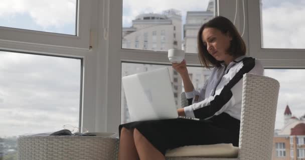 Con confianza elegante exitosa mujer de negocios sosteniendo la taza de café y mirando el monitor en el lugar de trabajo moderno con grandes ventanas — Vídeos de Stock