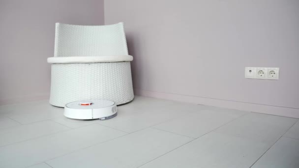 Robô redonda aspirador arrumar apartamento. aspirador de pó branco automaticamente dirigindo em torno da cadeira e piso de limpeza — Vídeo de Stock