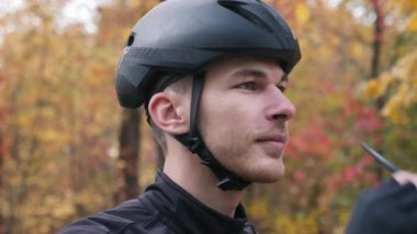 Motive olmuş siyah kasklı genç bisikletçi bisiklet sporundan önce spor gözlüğü takıyor. Ekstra yakın görüş. Sonbahar parkında bisiklet eğitimi. Erkek bisikleti. Triatlon konsepti. Yavaş çekim