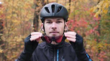 Sonbahar parkında profesyonel triatloncu. Genç çekici erkek bisikletçi antrenmana hazırlanıyor ve sonbahar ormanlarında gözlük takıyor. Yavaş çekim
