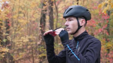 Siyah spor elbiseli ve kasklı profesyonel bir bisikletçi sonbahar parkında antrenmana hazırlanıyor ve gözlük takıyor. Sonbahar parkında bisiklet eğitimi. Yan görünüm, yavaş çekim