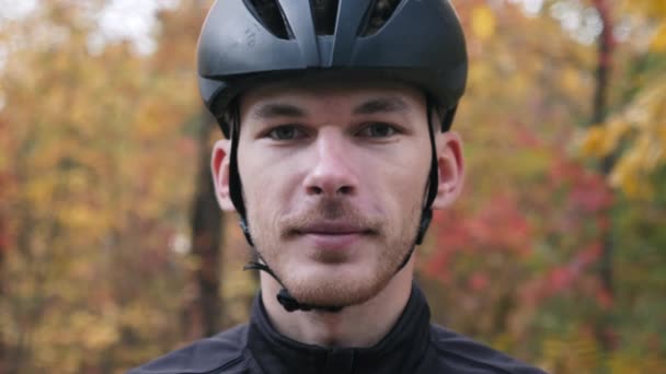 Portrait of young professional cyclist in fall beautiful forest. Extra close up view of male face in helmet puts on sport glasses before cycling training — Stock Video