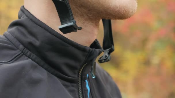 Vue de très près de l'homme cycliste ferme la fixation du casque. Cycliste professionnel masculin ferme le fermoir sur le casque dans le parc d'automne avant l'entraînement. Mouvement lent — Video