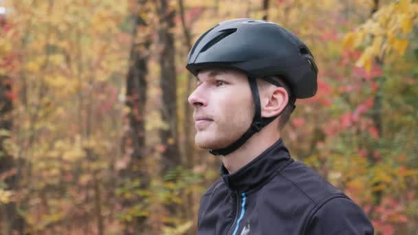 Porträt eines energischen jungen männlichen Radfahrers, der vor dem Training auf dem Fahrrad im Herbstpark eine Sportbrille aufsetzt. attraktiver kaukasischer Radrennfahrer, der sich auf das Training im Freien vorbereitet. Zeitlupe — Stockvideo