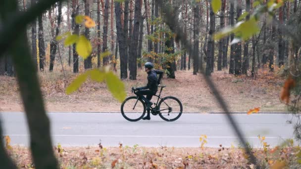 スマートフォンで自撮りを取るロードバイクとヘルメットの若いスタイリッシュなプロのサイクリスト。自転車に座って秋の公園で写真を撮るサイクリングアパレルの魅力的なハンサムな男 — ストック動画