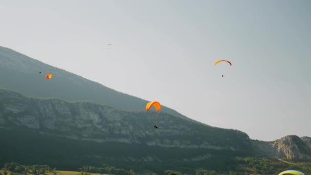 Narancs paraplanok repülnek az Alpok felett. Siklóernyő repül a kék ég és a hegyek az Alpokban. Siklóernyős leckék — Stock videók